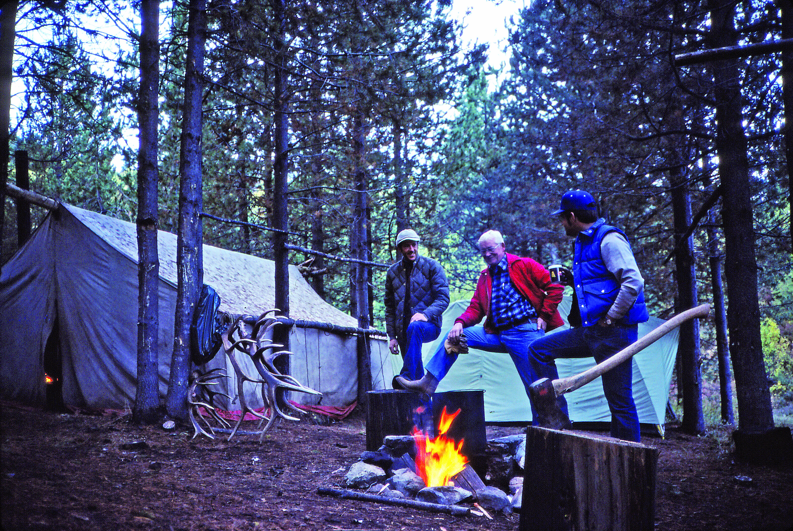 hunters standing around chopping wood outside their canvas wall tent