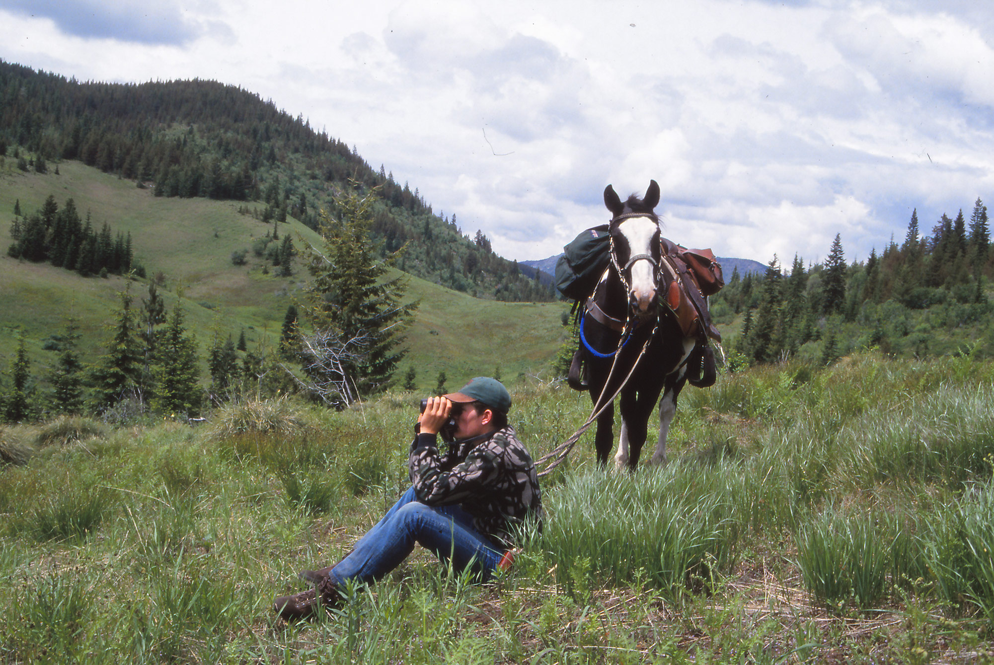 a hunter glassing for spring bears next to his horse.