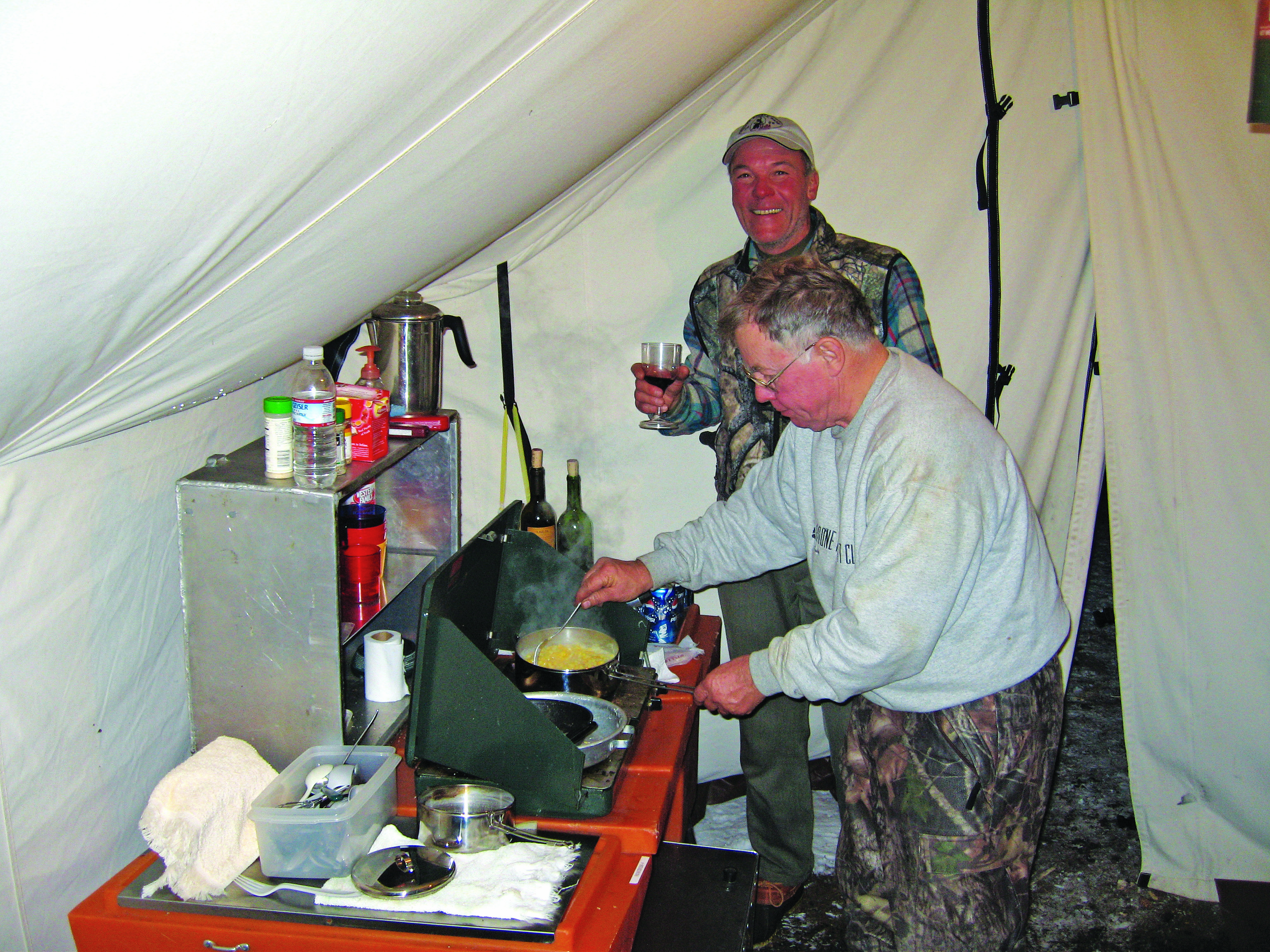 a couple of hunters enjoying a meal inside a tent