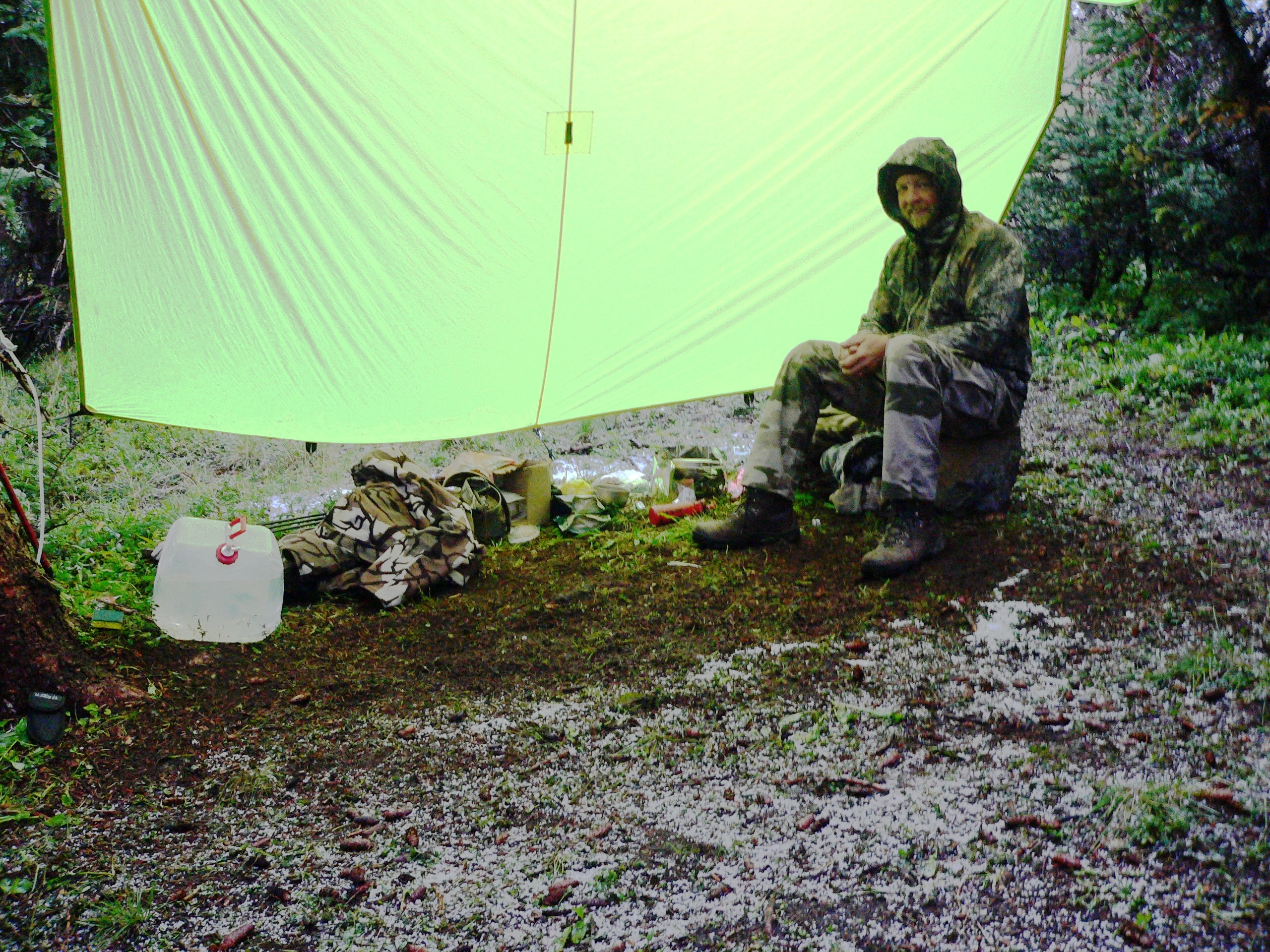 A bowhunter sitting under a shelter in the rain.